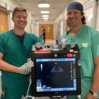 Two residents in scrubs smiling in front of an ultrasound image